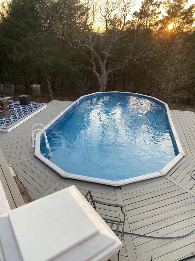 pool at dusk with an outdoor pool and a deck