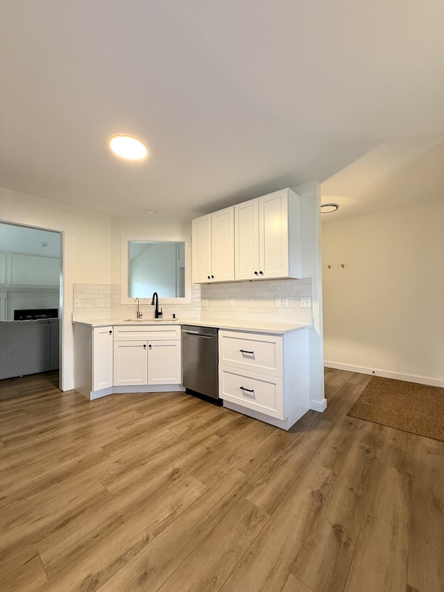 kitchen featuring stainless steel dishwasher, white cabinets, a sink, light countertops, and decorative backsplash