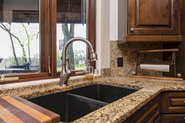 room details with light stone countertops, dark brown cabinetry, a sink, and tasteful backsplash