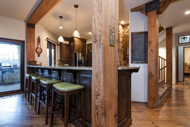 kitchen featuring a kitchen bar, wood finished floors, stainless steel fridge, and light stone counters