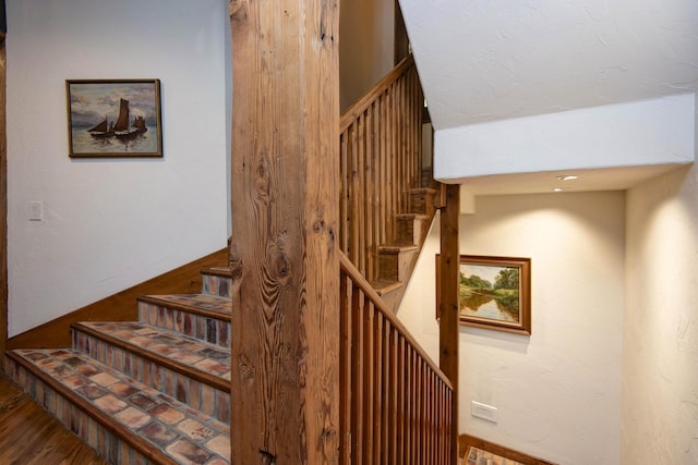 stairway with wood finished floors and a textured wall