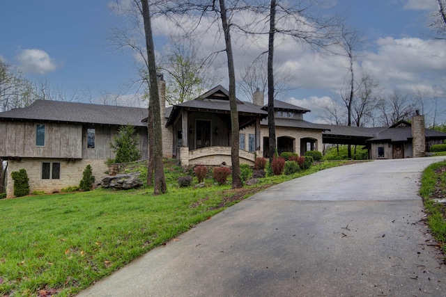 view of front facade featuring stone siding, a front yard, driveway, and a chimney