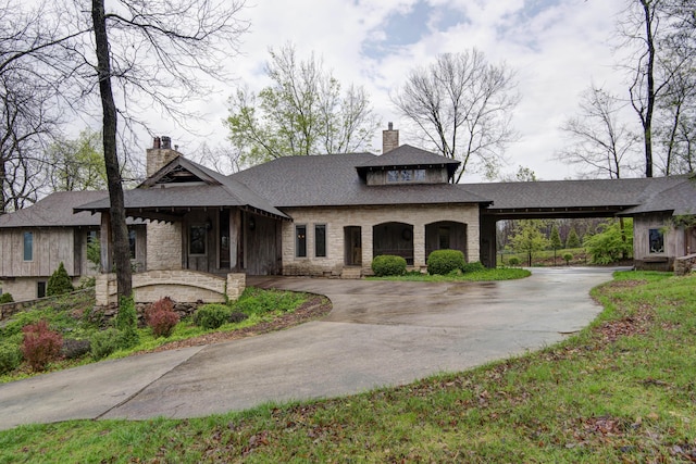 view of front facade featuring a chimney, a shingled roof, stone siding, and curved driveway