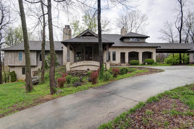 view of front of house with stone siding, a chimney, a front yard, a shingled roof, and curved driveway