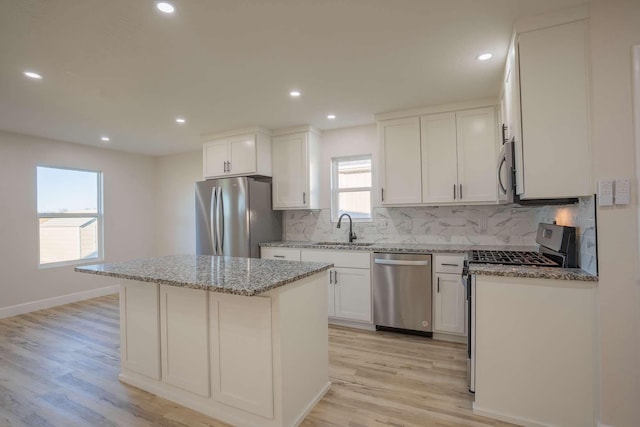 kitchen with backsplash, a kitchen island, light stone countertops, appliances with stainless steel finishes, and a sink