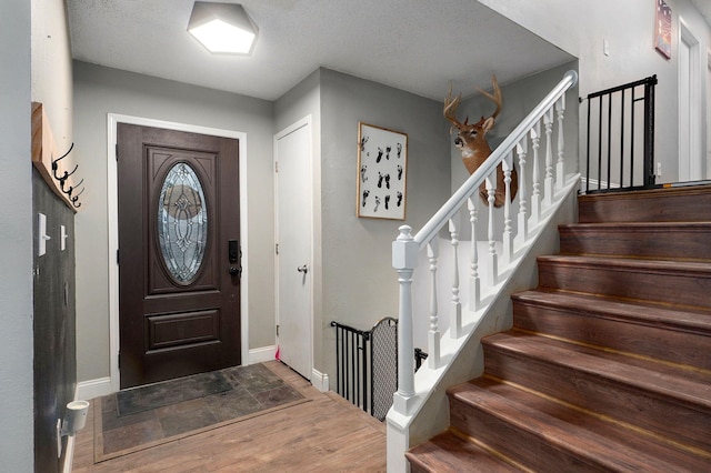 entrance foyer with a textured ceiling, wood finished floors, baseboards, and stairway