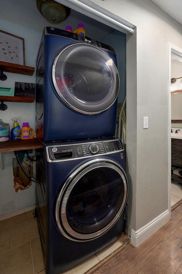 laundry area with baseboards, laundry area, wood finished floors, and stacked washer and clothes dryer