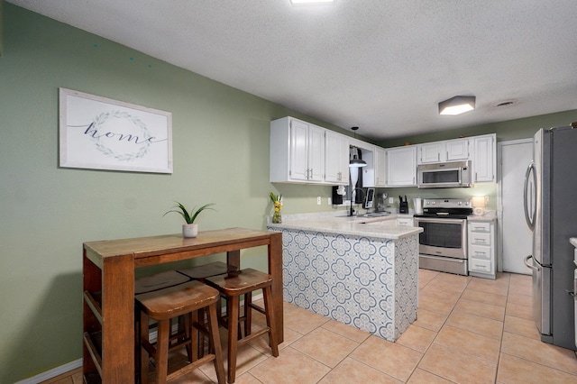 kitchen featuring a peninsula, light tile patterned floors, light countertops, stainless steel appliances, and a sink
