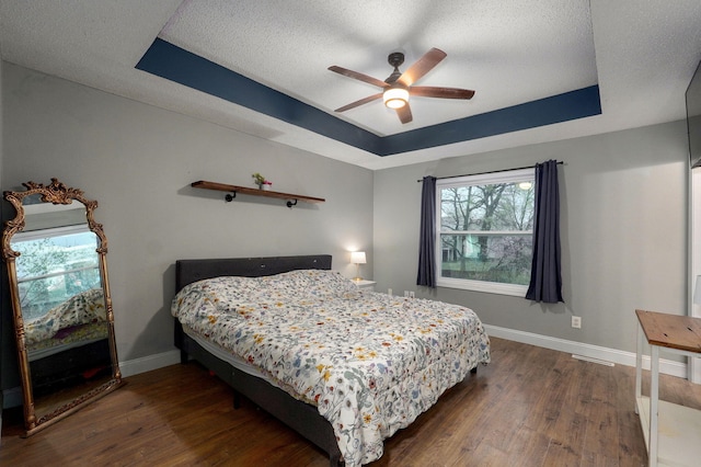 bedroom with a tray ceiling, a textured ceiling, wood finished floors, and baseboards