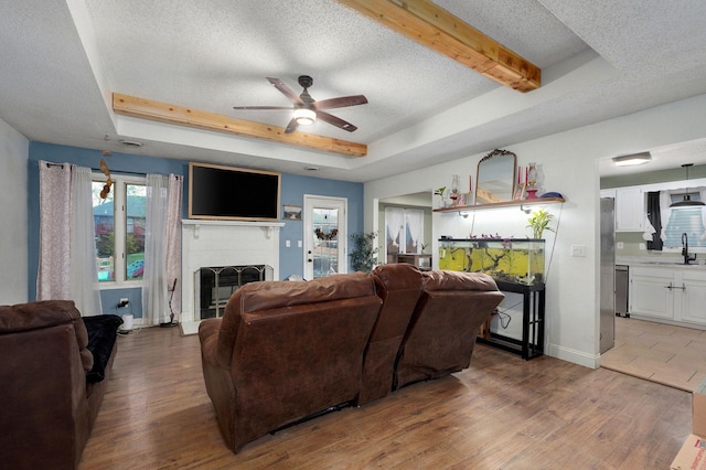 living room with a tray ceiling, a brick fireplace, a ceiling fan, and wood finished floors