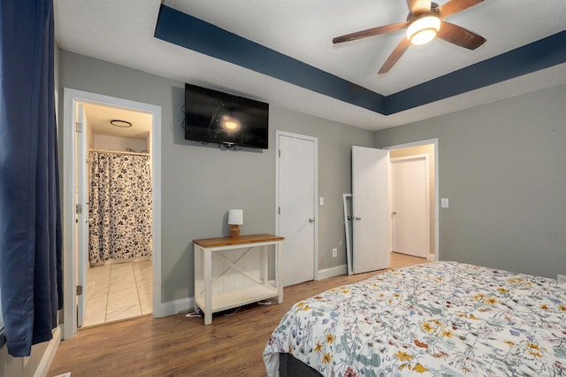 bedroom with ensuite bathroom, a tray ceiling, baseboards, and wood finished floors
