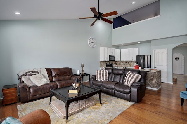 living area with arched walkways, a ceiling fan, wood finished floors, lofted ceiling, and baseboards