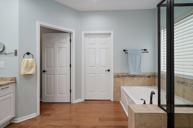 full bath with vanity, a garden tub, and wood finished floors