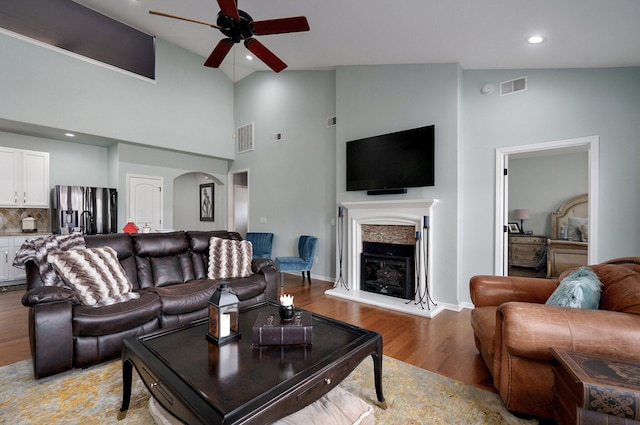 living room with light wood-style flooring, ceiling fan, a fireplace with raised hearth, and visible vents