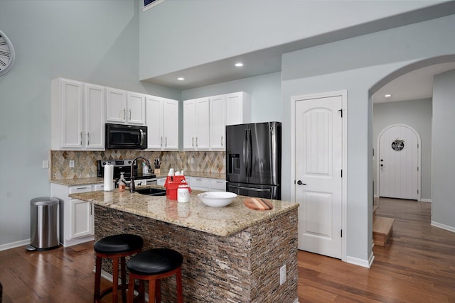 kitchen featuring dark wood-style flooring, white cabinetry, decorative backsplash, arched walkways, and black appliances