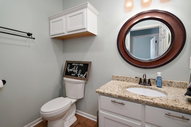 half bathroom featuring toilet, vanity, and baseboards