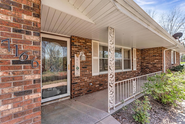 view of exterior entry featuring covered porch and brick siding