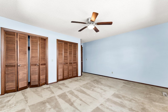 unfurnished bedroom featuring baseboards, light carpet, a textured ceiling, multiple closets, and ceiling fan