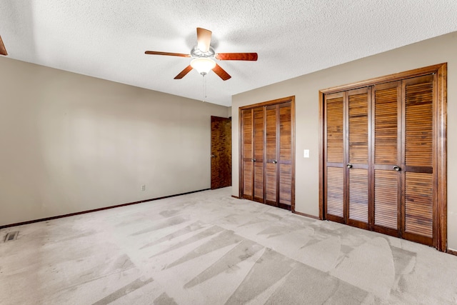 unfurnished bedroom with baseboards, ceiling fan, a textured ceiling, multiple closets, and carpet flooring