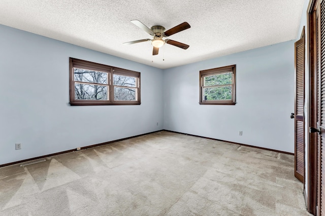 carpeted spare room featuring visible vents, baseboards, a ceiling fan, and a textured ceiling