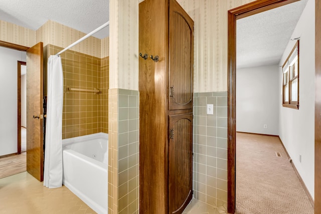 full bath with shower / tub combo, a textured ceiling, wallpapered walls, and a wainscoted wall