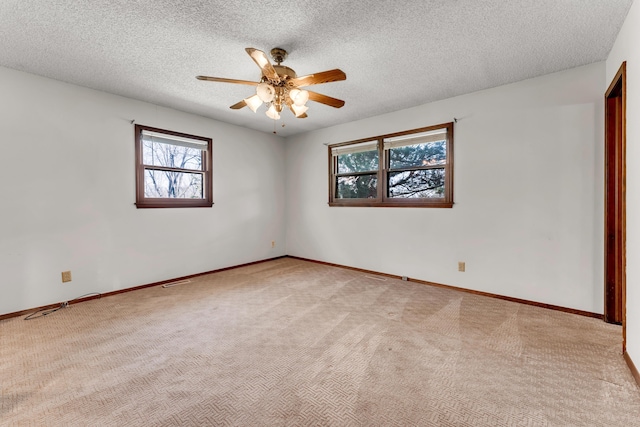 spare room with ceiling fan, a textured ceiling, light colored carpet, visible vents, and baseboards