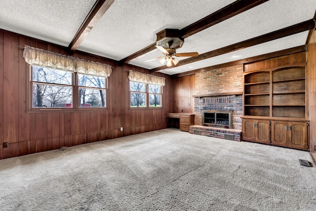 unfurnished living room with beamed ceiling, a textured ceiling, a ceiling fan, carpet floors, and wooden walls
