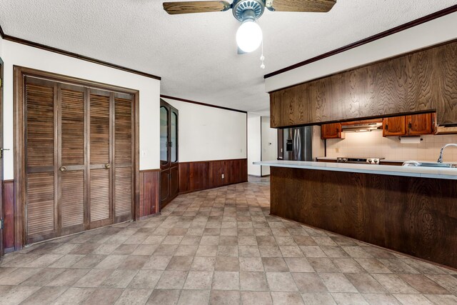 kitchen featuring stainless steel refrigerator with ice dispenser, a peninsula, light countertops, and a wainscoted wall
