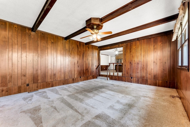 carpeted empty room with wood walls, a textured ceiling, beamed ceiling, and ceiling fan