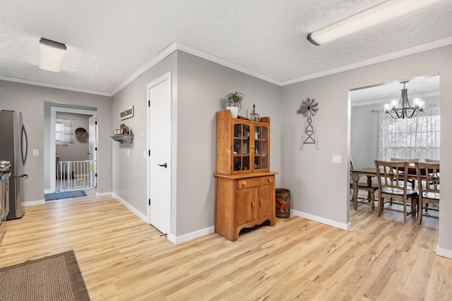 corridor featuring a notable chandelier, a textured ceiling, ornamental molding, and light wood-style flooring