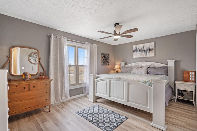 bedroom with baseboards, light wood-style floors, a textured ceiling, and a ceiling fan
