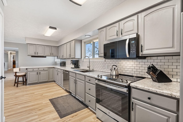 kitchen with light wood-style flooring, backsplash, gray cabinetry, stainless steel appliances, and a sink