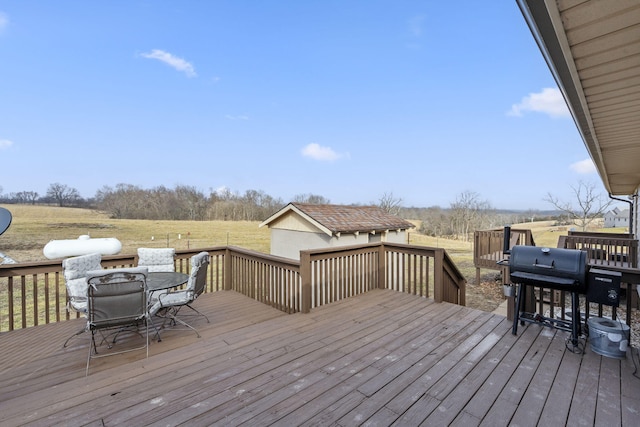 wooden terrace with a rural view, outdoor dining space, a grill, and an outdoor structure