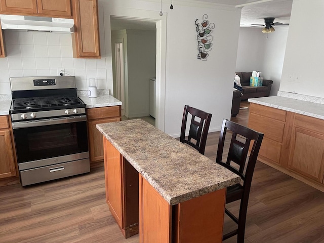 kitchen with decorative backsplash, light wood-type flooring, under cabinet range hood, and gas stove