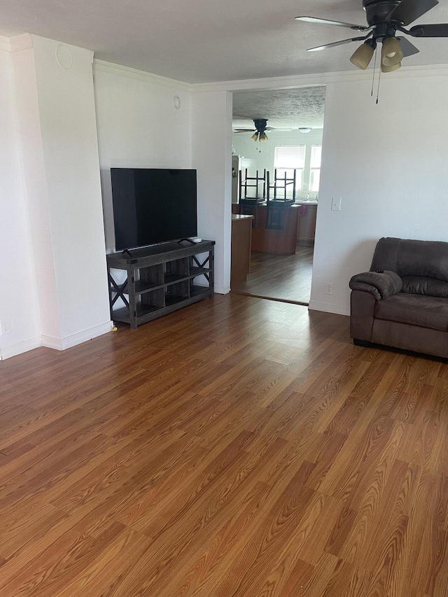 living area featuring ceiling fan, baseboards, ornamental molding, and wood finished floors