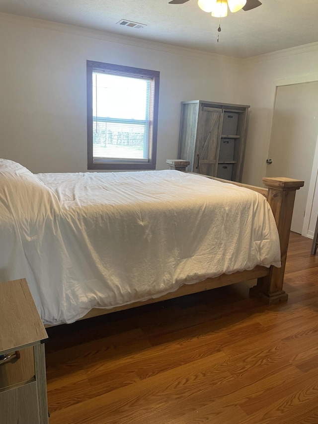 bedroom featuring crown molding, wood finished floors, ceiling fan, and visible vents