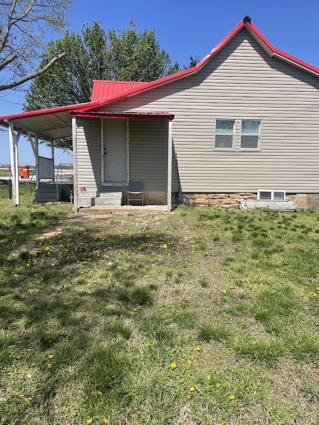 rear view of property with metal roof, entry steps, and a lawn
