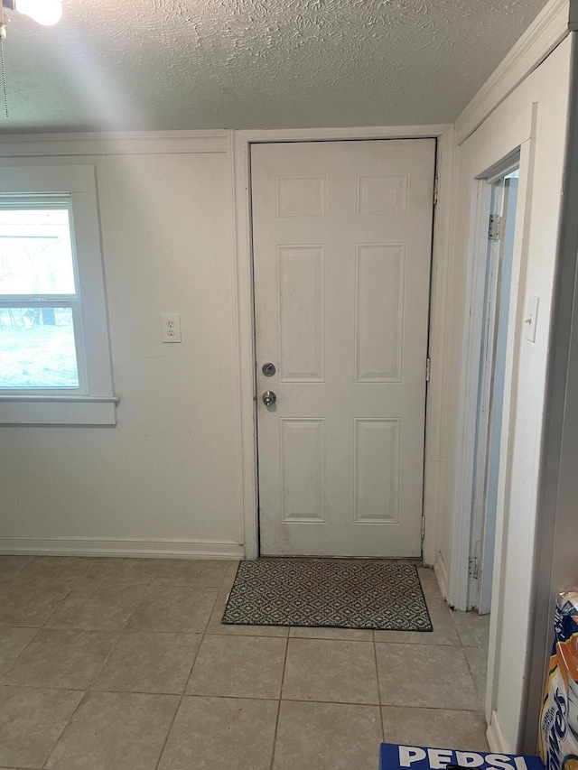 entryway with light tile patterned floors, a textured ceiling, and baseboards