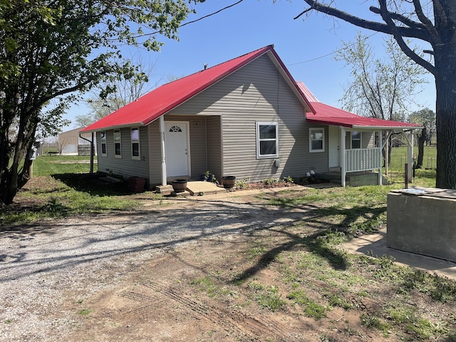 view of front of home with dirt driveway, covered porch, and metal roof