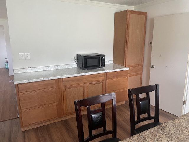 kitchen featuring dark wood-style flooring, light countertops, black microwave, and crown molding