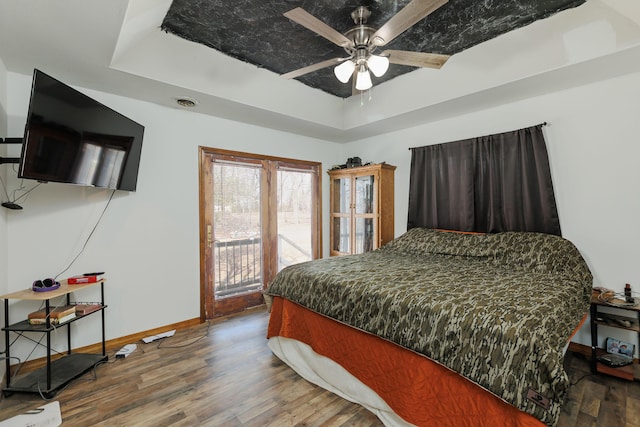 bedroom with baseboards, a raised ceiling, a ceiling fan, wood finished floors, and access to exterior