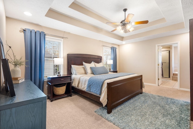 bedroom featuring a tray ceiling, baseboards, ensuite bath, and light carpet