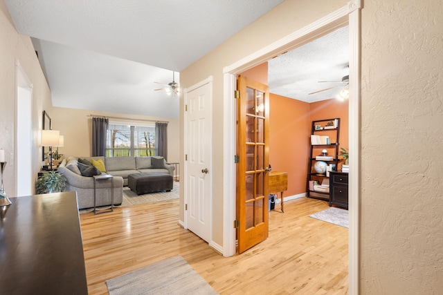 hallway with a textured ceiling, wood finished floors, a textured wall, and vaulted ceiling