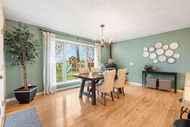 dining room with a wood stove, a textured ceiling, a chandelier, light wood finished floors, and baseboards