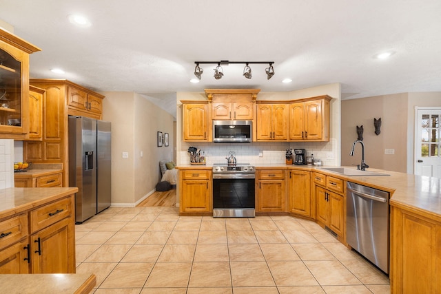 kitchen with light tile patterned floors, glass insert cabinets, decorative backsplash, stainless steel appliances, and a sink