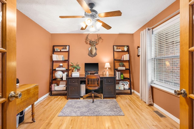 home office with light wood-style floors, visible vents, baseboards, and ceiling fan