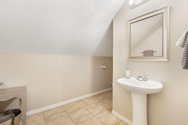 bathroom featuring baseboards, vaulted ceiling, tile patterned floors, a textured ceiling, and a sink