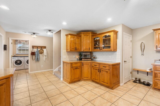 kitchen with independent washer and dryer, tasteful backsplash, glass insert cabinets, and brown cabinetry