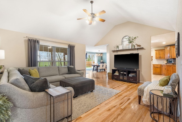 living area featuring high vaulted ceiling, light wood finished floors, and ceiling fan with notable chandelier