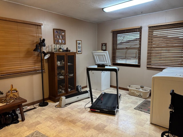 exercise room featuring washer / clothes dryer, baseboards, a textured ceiling, and light floors